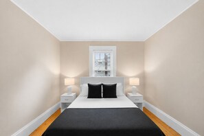 A bedroom with a bed, two bedside tables, a window, and a nightstand.