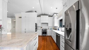 Una cocina moderna con muebles blancos, electrodomésticos de acero inoxidable y encimera de mármol.
