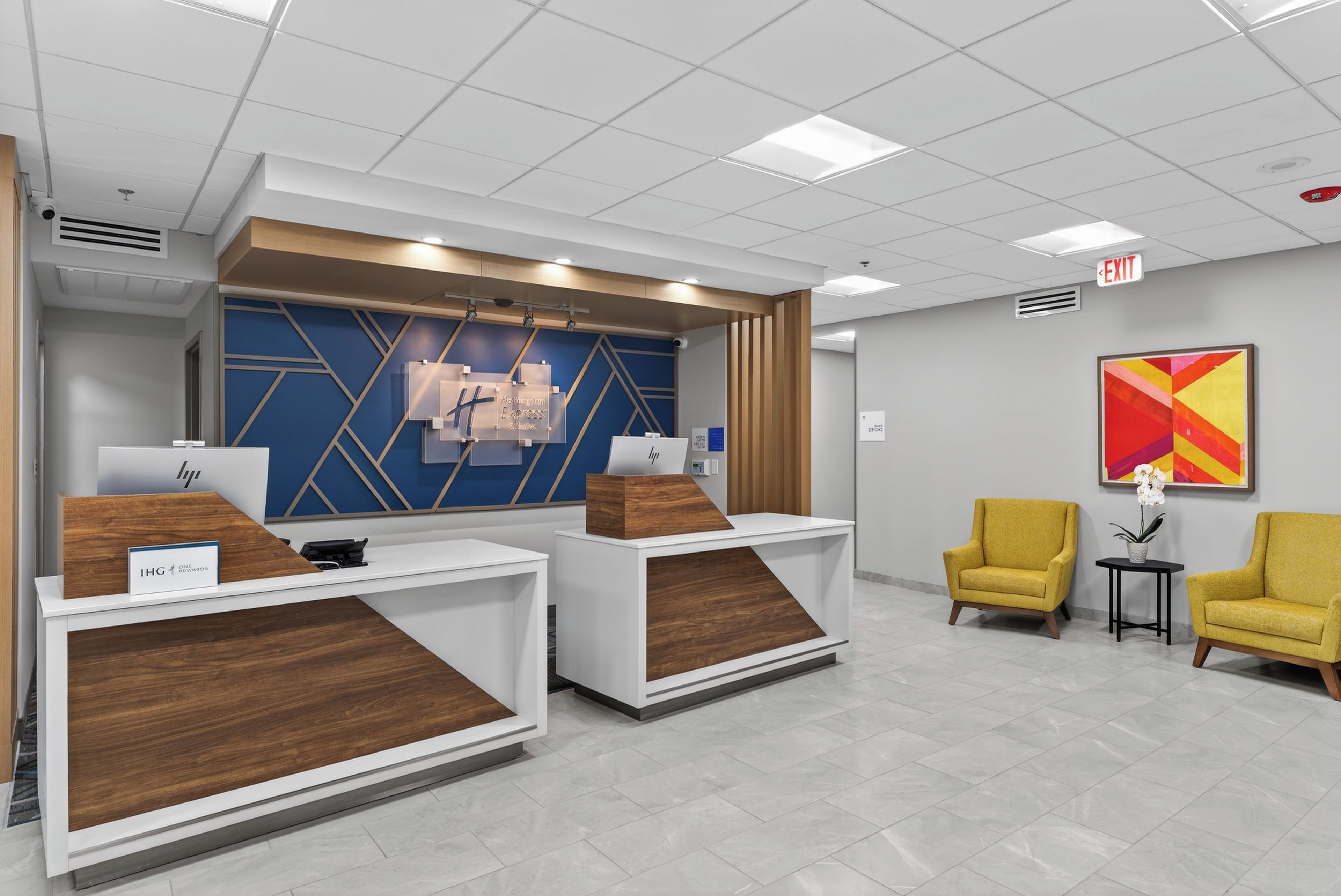 Un espace d’accueil comprenant deux comptoirs de réception, un mur décoré d’un motif géométrique bleu et deux fauteuils jaunes.