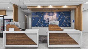 Un mostrador de recepción con un diseño geométrico azul en la pared, un letrero de Holiday Inn Express y un refrigerador con bebidas.
