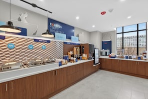 Zona esmorzar moderna amb un mostrador que ofereix menjar calent, cereals i fruita.