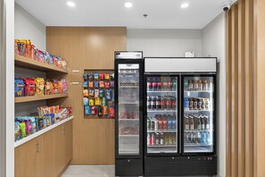 A compact kitchenette with a refrigerator, shelves stocked with snacks, and a beverage dispenser. - Holiday Inn Express and Suites Chicago West Oak Park by IHG (Oak Park)