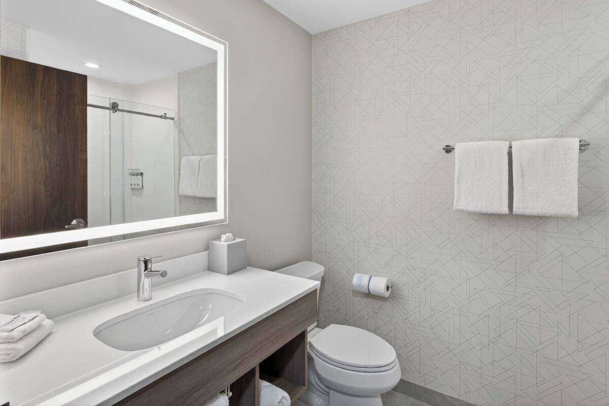 Un baño moderno con un espejo grande, un lavamanos, un inodoro y una ducha.