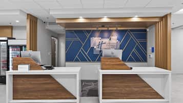 A reception desk with a blue geometric wall design, a Holiday Inn Express sign, and a vending machine to the left.