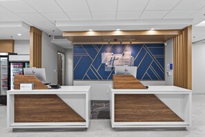Un comptoir d’accueil avec un mur décoré de motifs géométriques bleus, une enseigne Holiday Inn Express et un distributeur automatique situé à gauche.