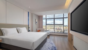 Een moderne hotelkamer met een groot bed, stadszicht door grote ramen en een flatscreen televisie.