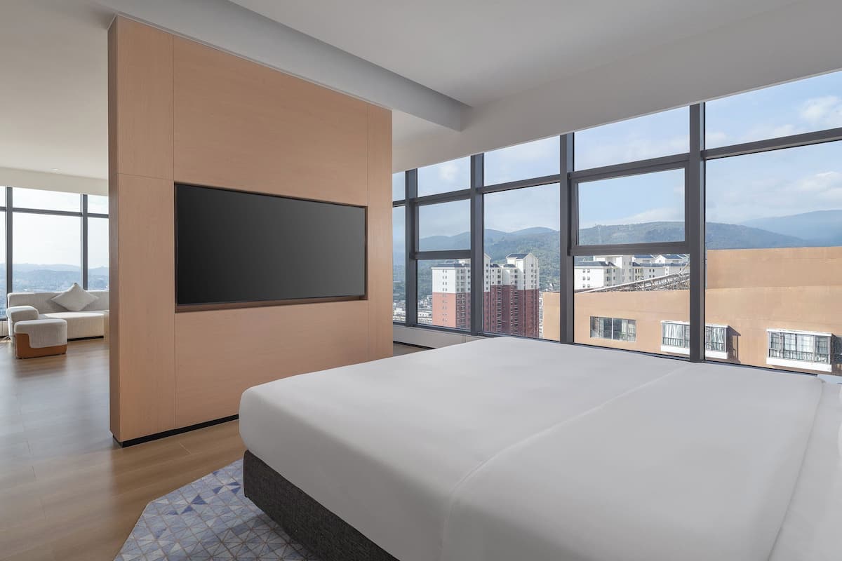 Ein modernes Hotelzimmer mit einem großen Bett, einem wandmontierten Flachbildfernseher und einem großen Fenster mit Blick auf die Stadt.