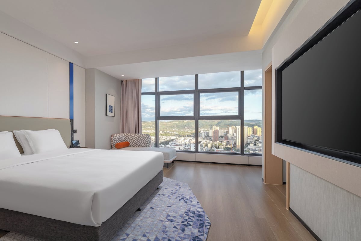Ein modernes Hotelzimmer mit einem großen Bett, einer Sitzecke und Blick auf die Stadt durch große Fenster.