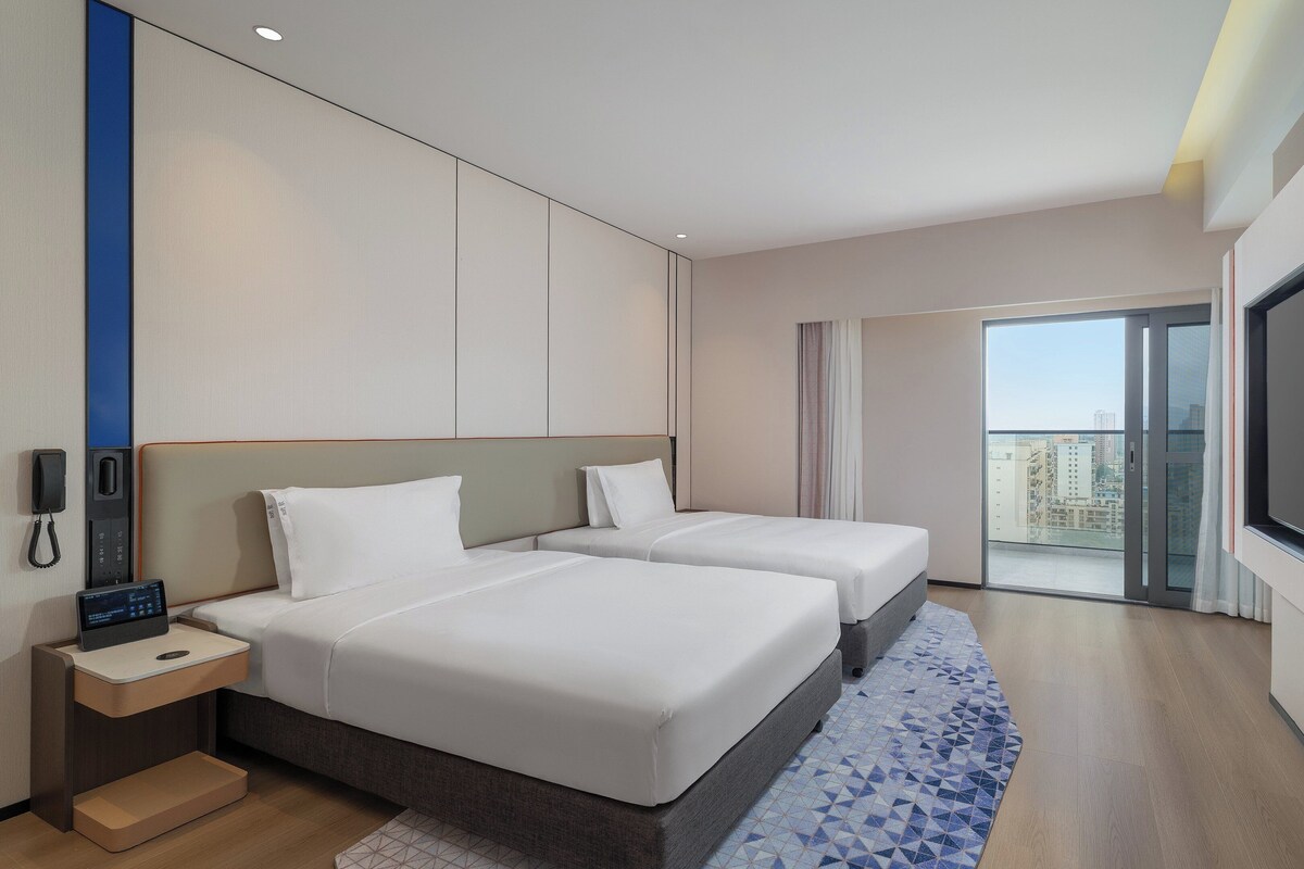 Een hotelkamer met twee bedden, een bureau met telefoon, een televisie en een balkon met uitzicht over de stad.
