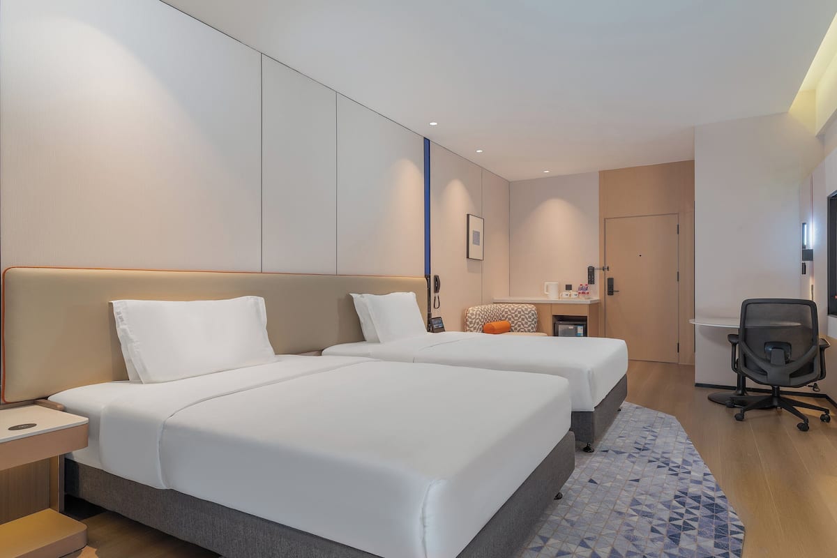 Ein Hotelzimmer mit zwei Betten, einem Schreibtisch, einem Stuhl, einem Fernseher und einer kleinen Küchenzeile.