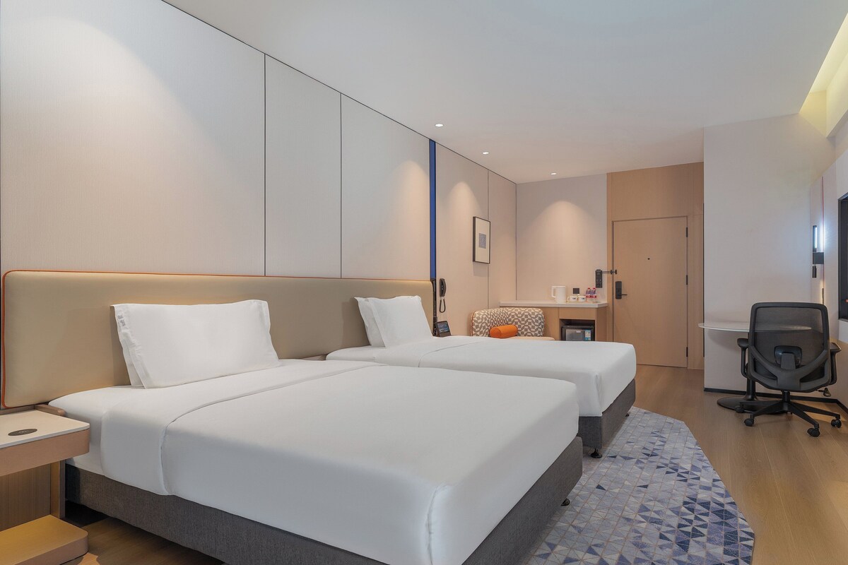 Een hotelkamer met twee bedden, een bureau, een stoel, een televisie en een kleine kitchenette.