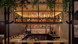 Zona de bar con varias estanterías llenas de botellas, una barra larga y asientos.