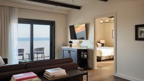 Una habitación de hotel moderna con balcón, un sofá, una mesa de centro con libros, un escritorio con lámpara y una cama.