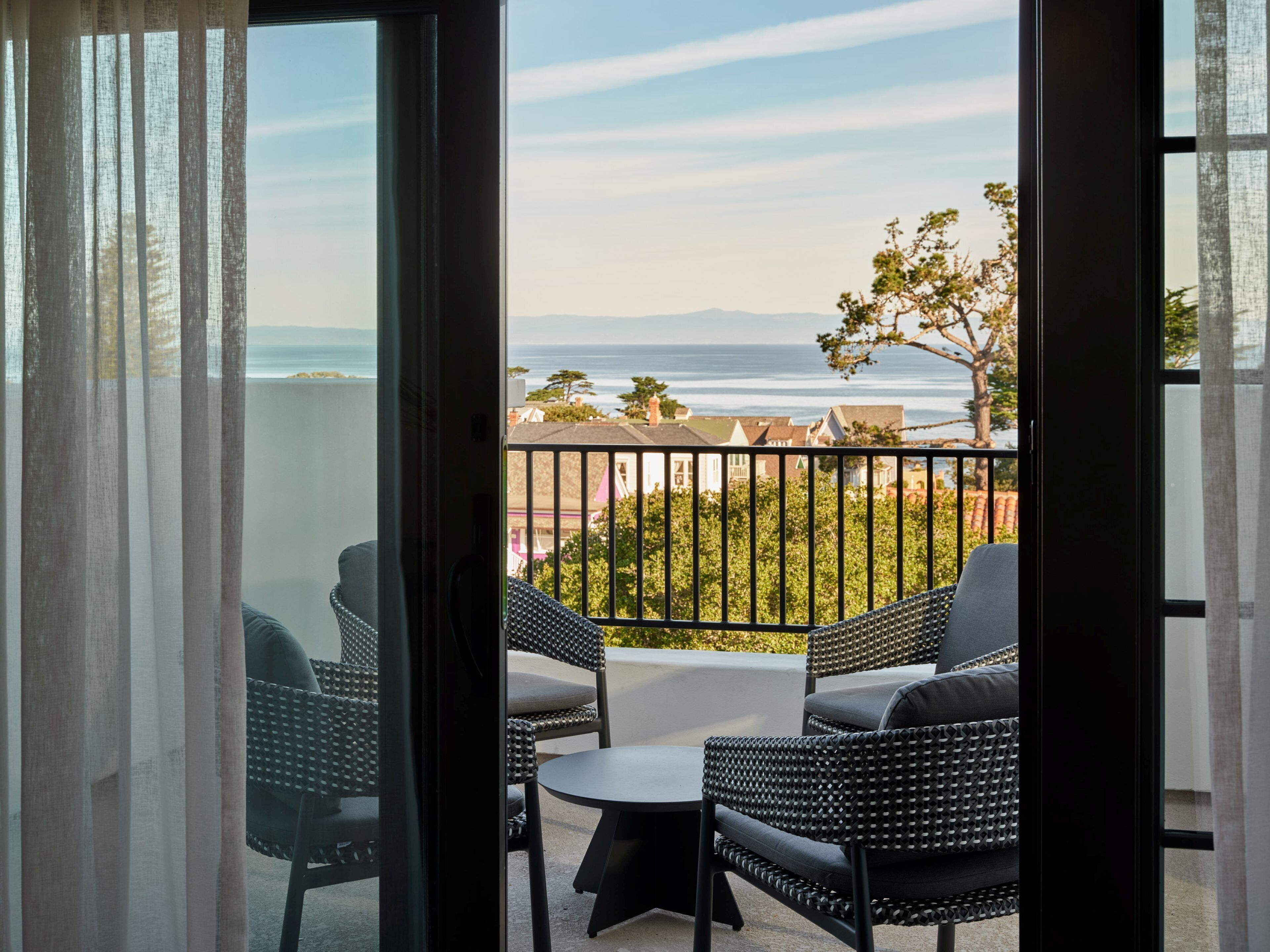 A balcony with wicker furniture, a view of the sea, and a tree.