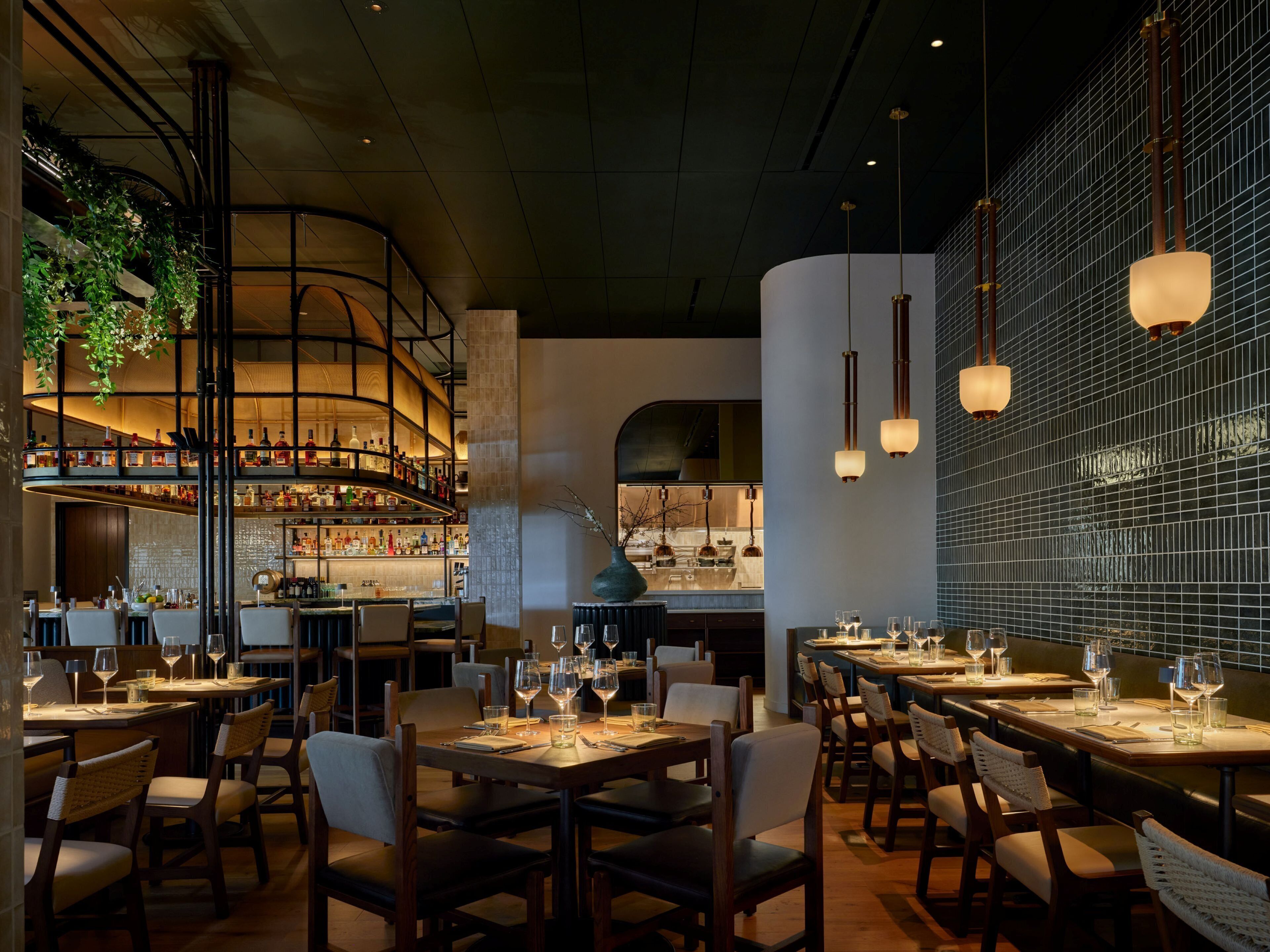A restaurant with a bar area, multiple dining tables, and hanging lights.