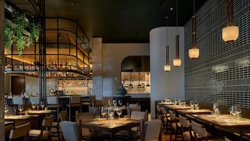 A restaurant with a bar area, multiple dining tables, and hanging lights.