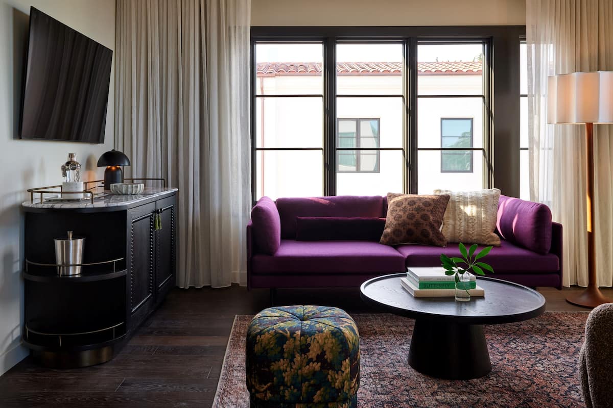 A modern living room with a purple sofa, a round coffee table, and a TV mounted on the wall.