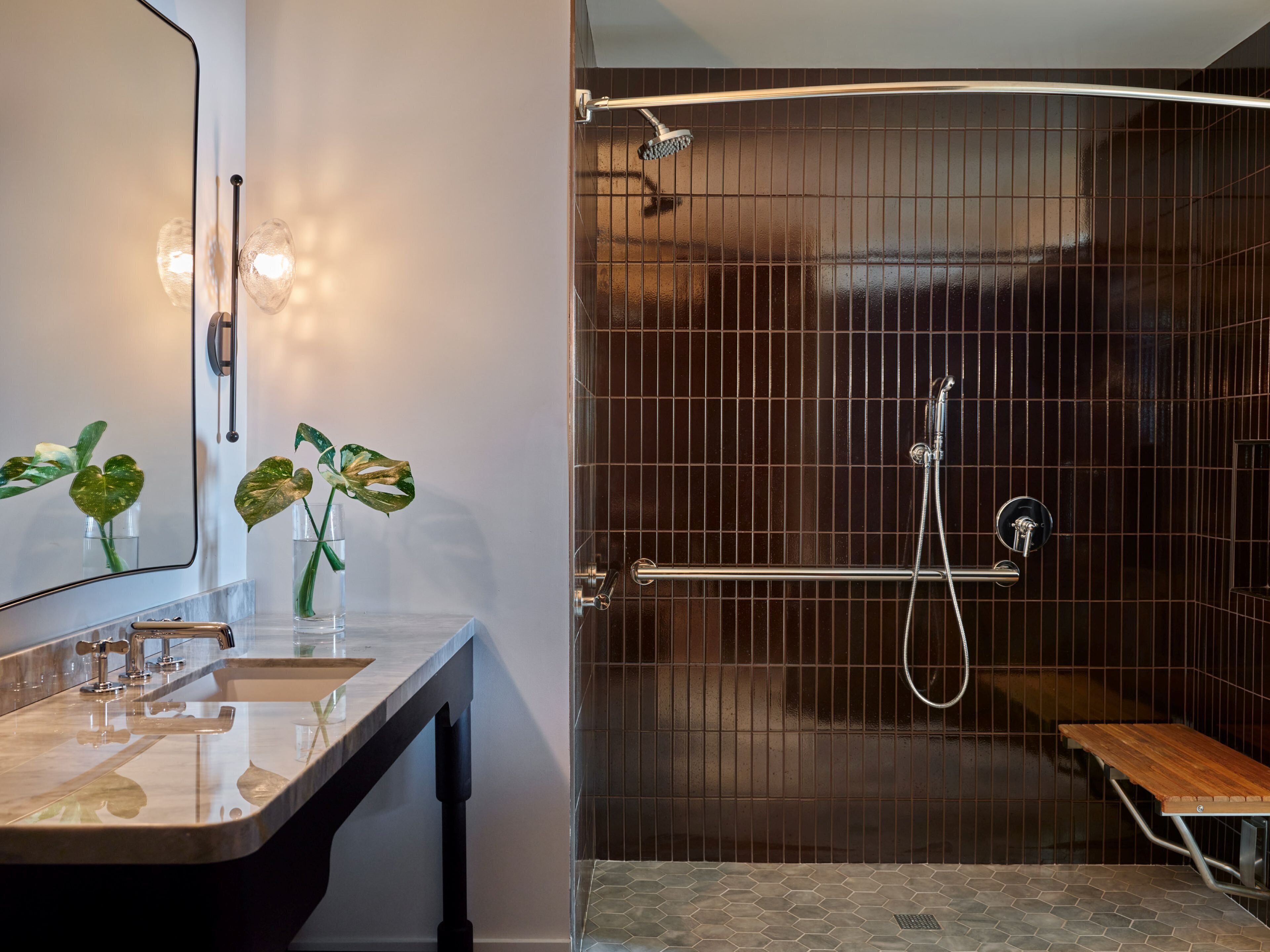 A modern bathroom with a vanity, a shower with a glass door, and a small wooden bench.