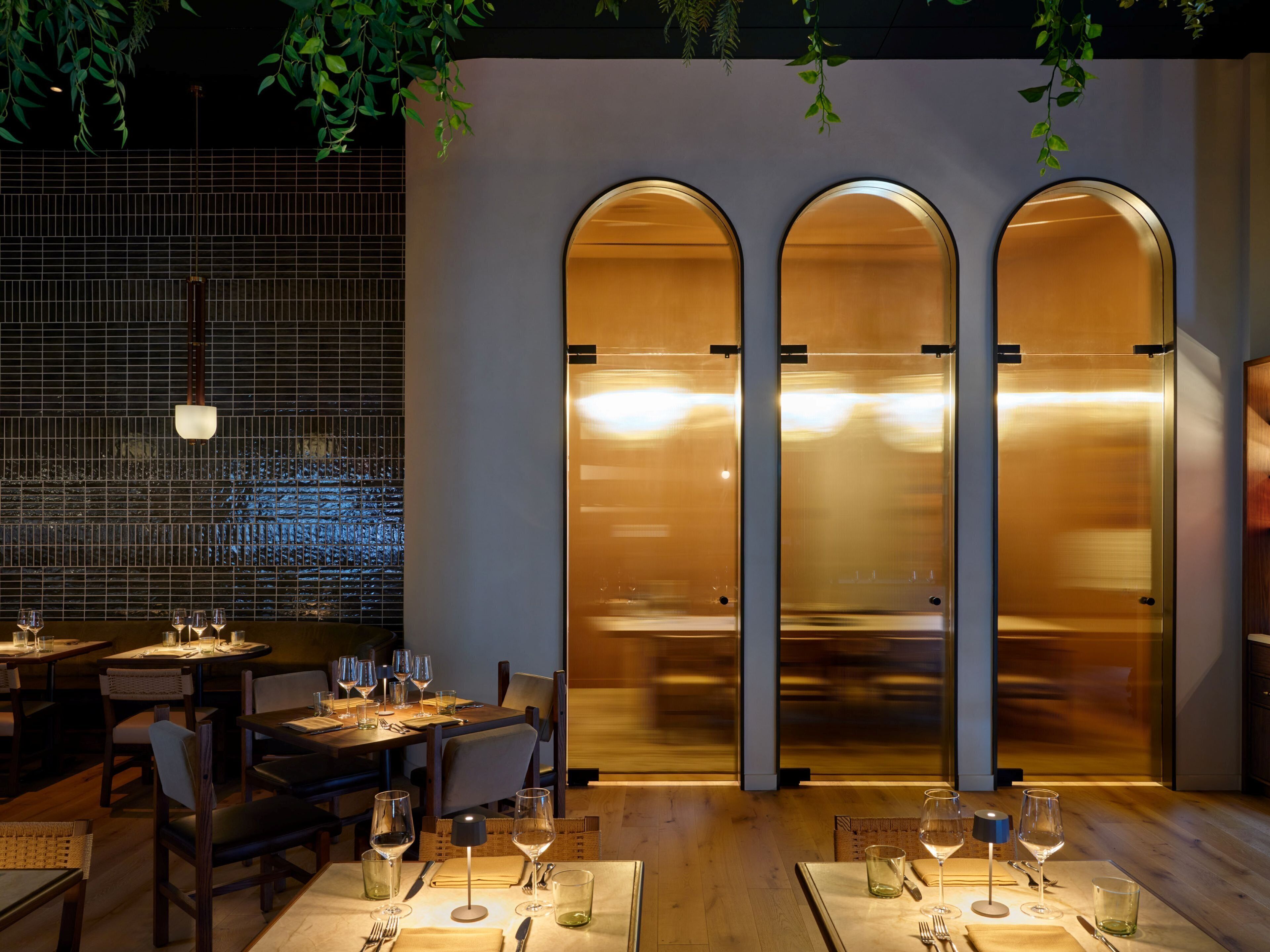 L’intérieur d’un restaurant, avec des tables dressées pour le service, un mur recouvert de carreaux et un ascenseur moderne.