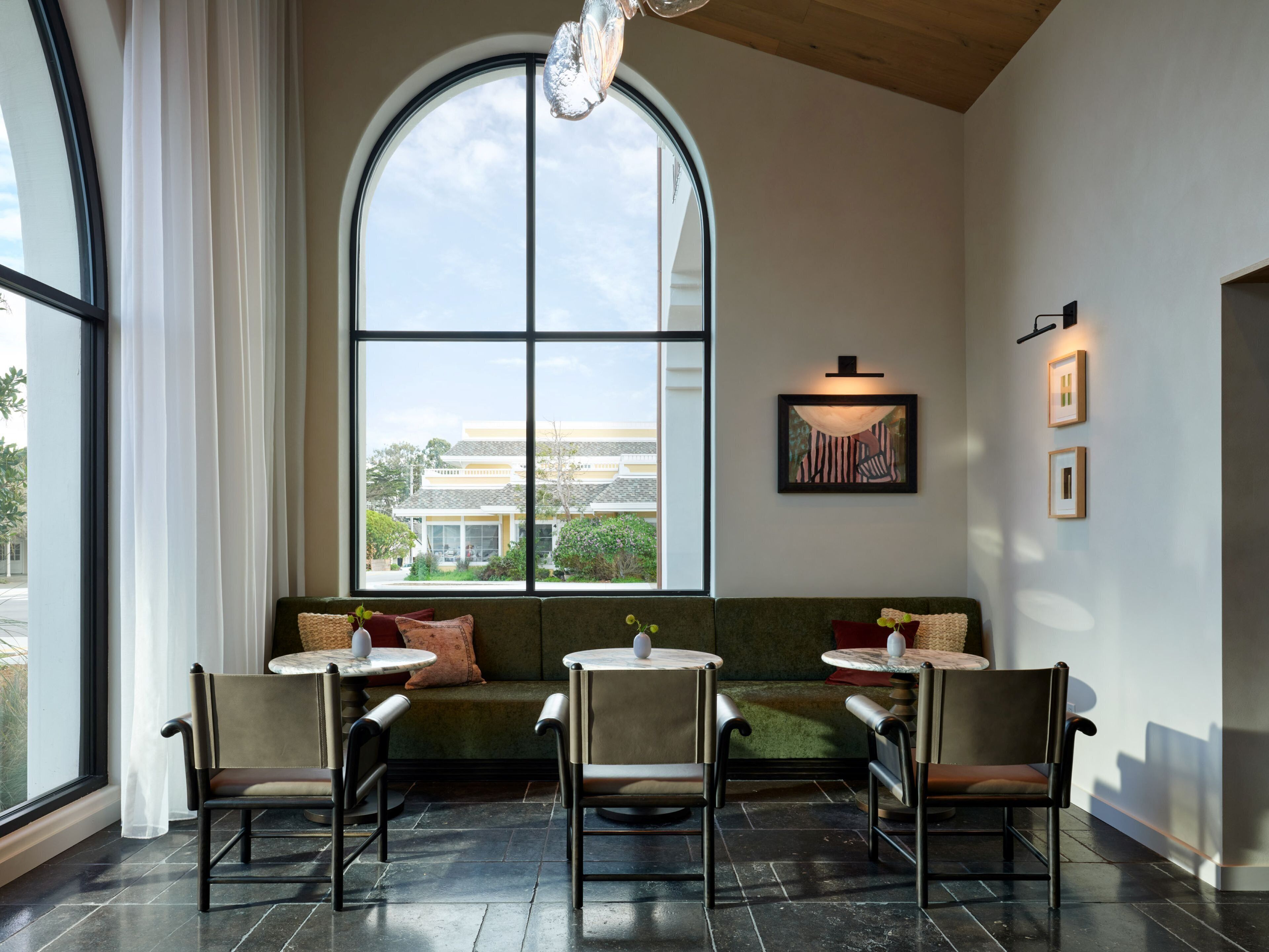 A modern interior with a large arched window, a green sofa, two chairs, and a table.