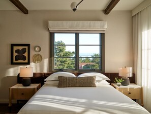 A bedroom with a large bed, two bedside tables with lamps, a window with a view of trees and a building, and a ceiling fan. - Kimpton Mirador Pacific Grove Monterey by IHG (Pacific Grove)
