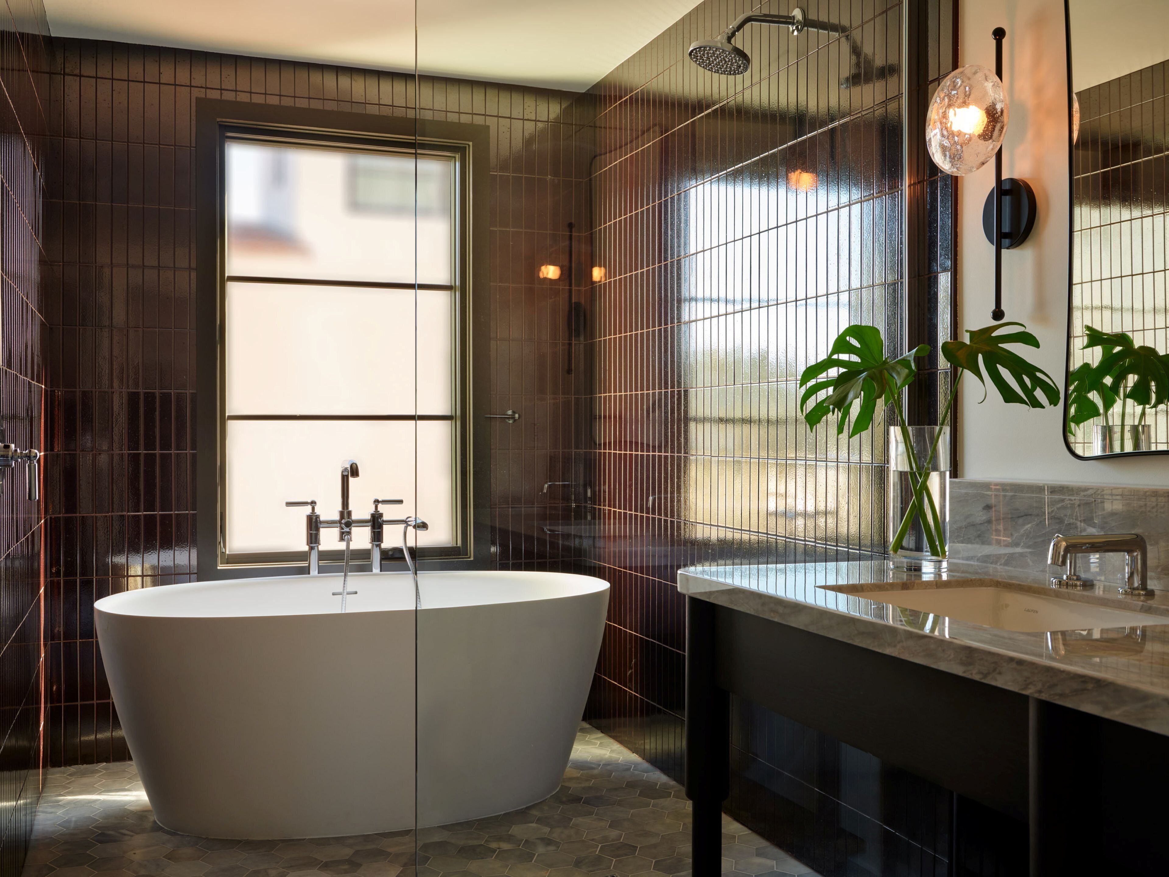 A modern bathroom with a freestanding bathtub, a large mirror, and a potted plant.