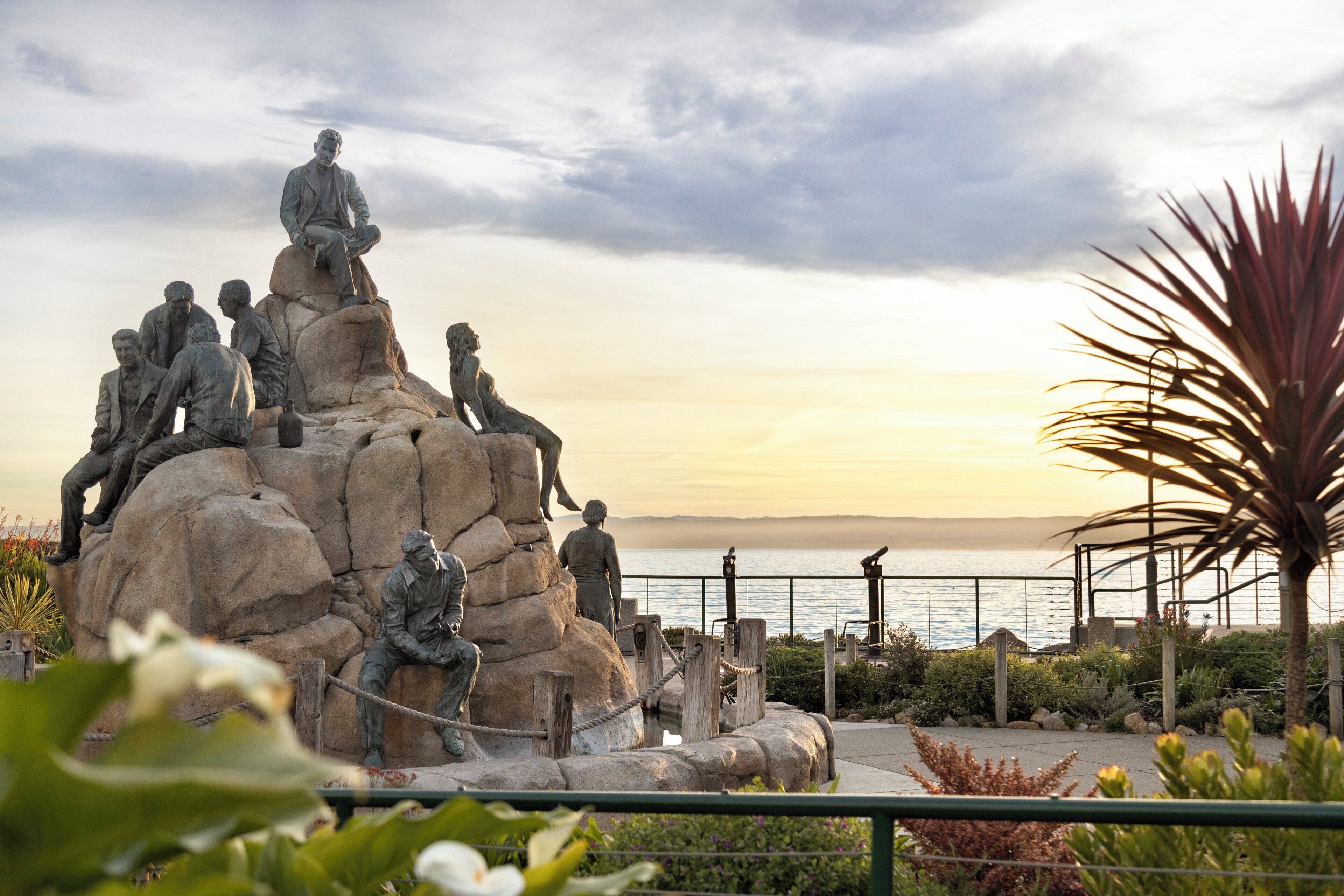 Une sculpture représentant des personnages, placée sur une formation rocheuse et offrant une vue sur la mer.