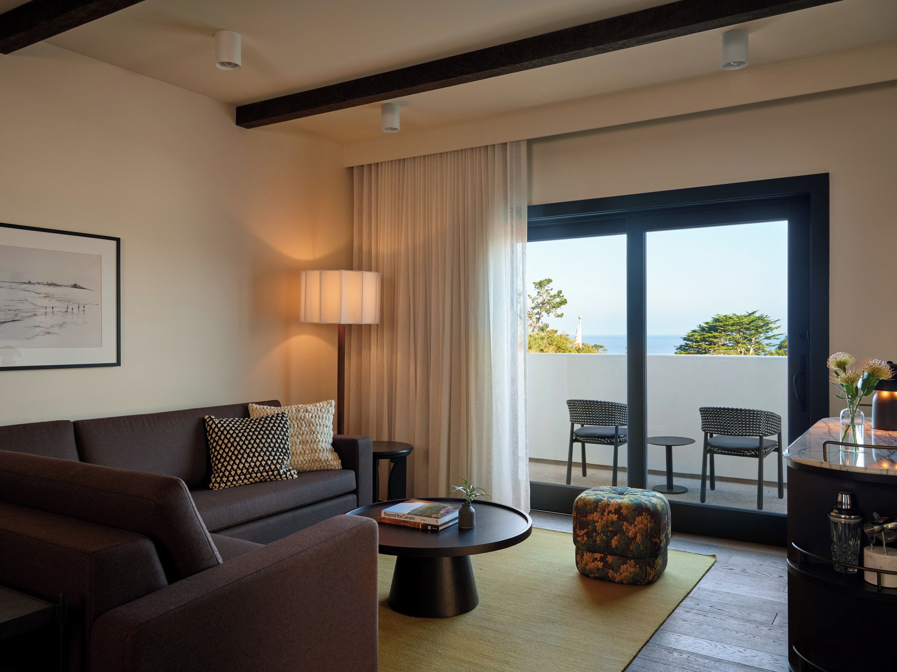 Una sala de estar moderna con un sofá, una mesa de centro y vistas al exterior a través de un amplio ventanal corredero.