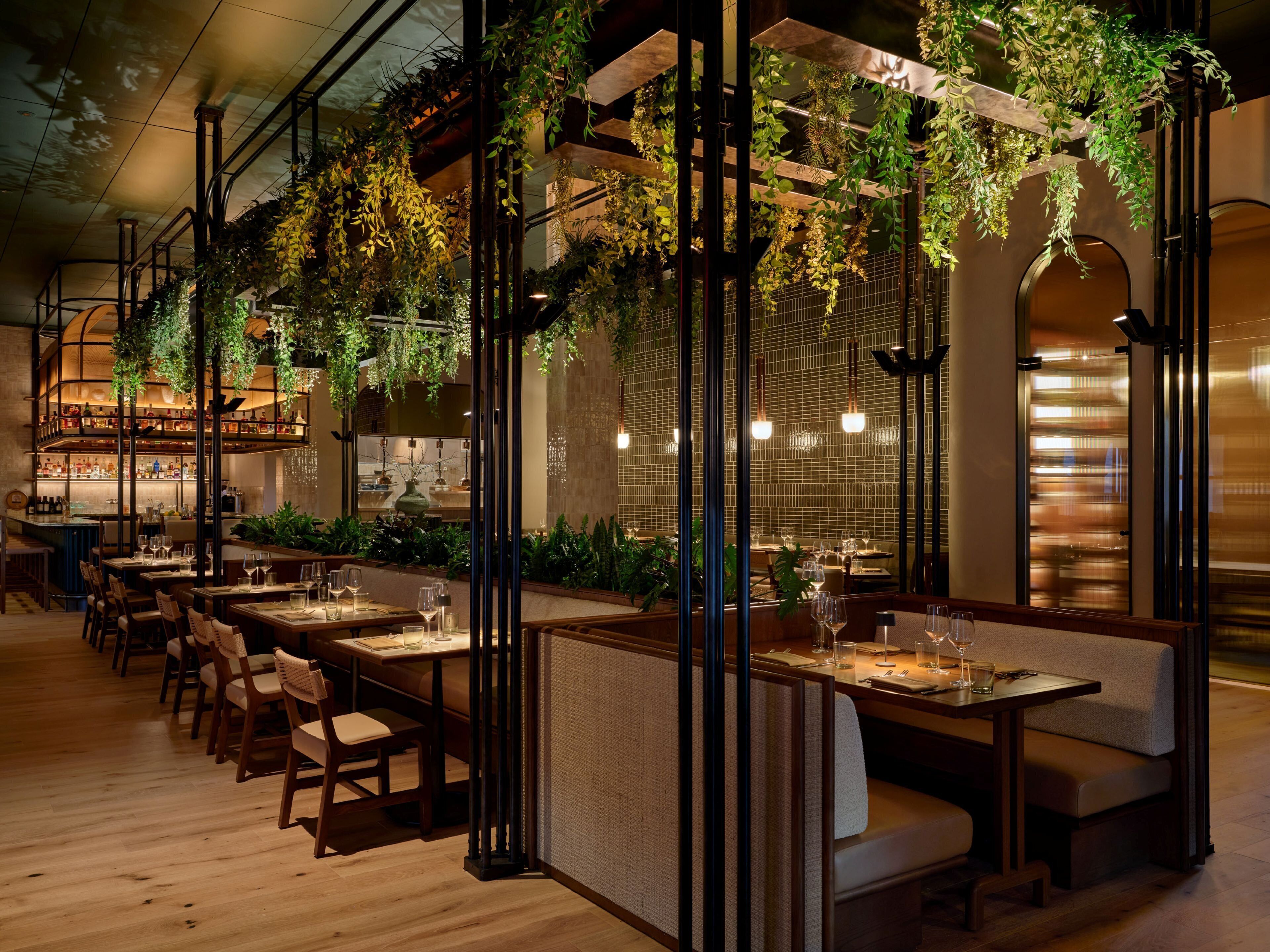 Un restaurante con mesas y cabinas de madera, plantas colgantes y una zona de bar.