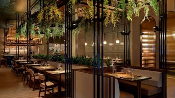 Un restaurante con mesas y cabinas de madera, plantas colgantes y una zona de bar.