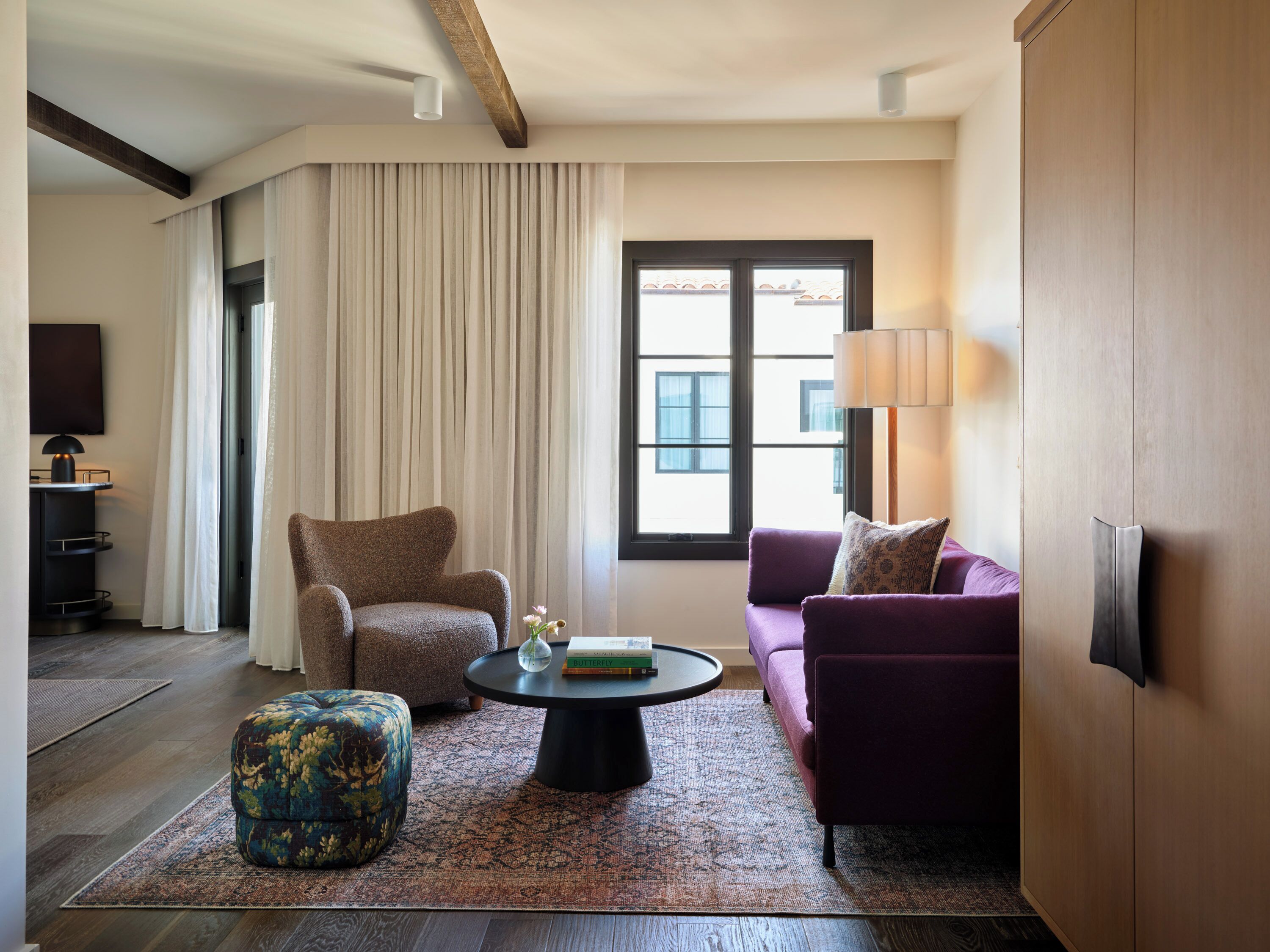 A modern living room with a brown armchair, a purple sofa, a round coffee table, and a patterned rug.