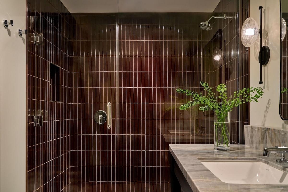 A modern bathroom with a glass-enclosed shower, a marble sink, and a potted plant.