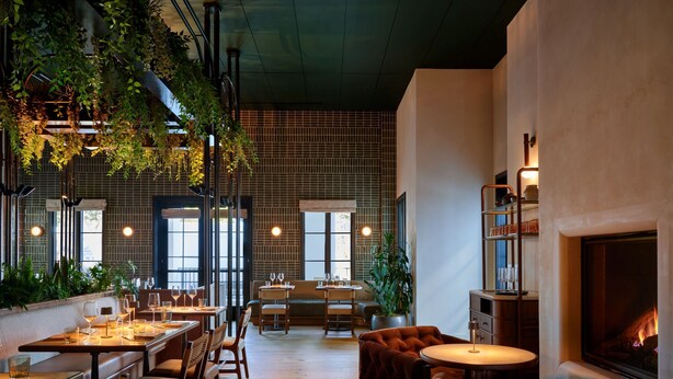Un restaurante con mesas y sillas de madera, una chimenea y plantas colgantes.