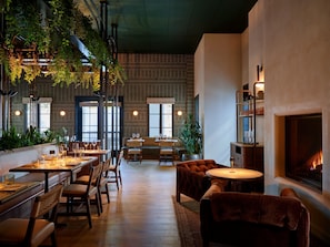 Un restaurante con mesas y sillas de madera, una chimenea y plantas colgantes.