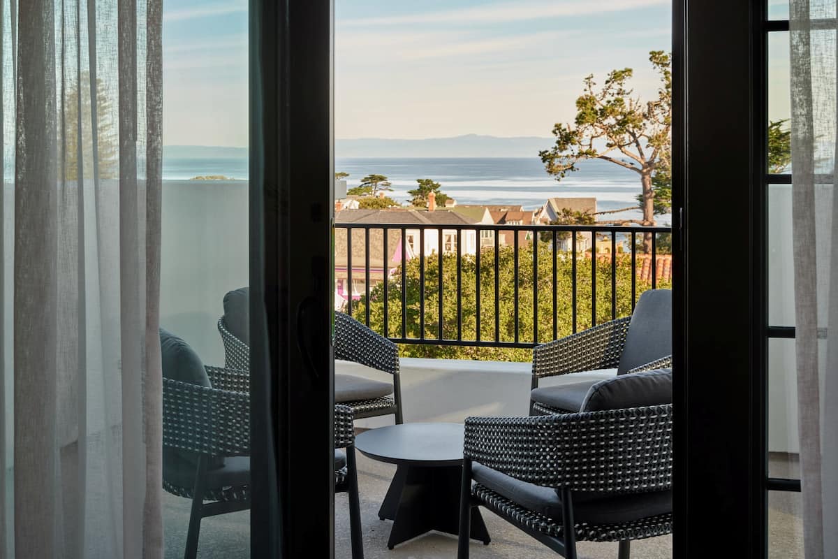 A balcony with wicker furniture, a view of the sea, and a tree.