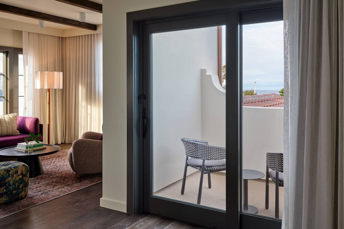 A modern hotel room with a sliding glass door leading to a balcony with a view of the cityscape.