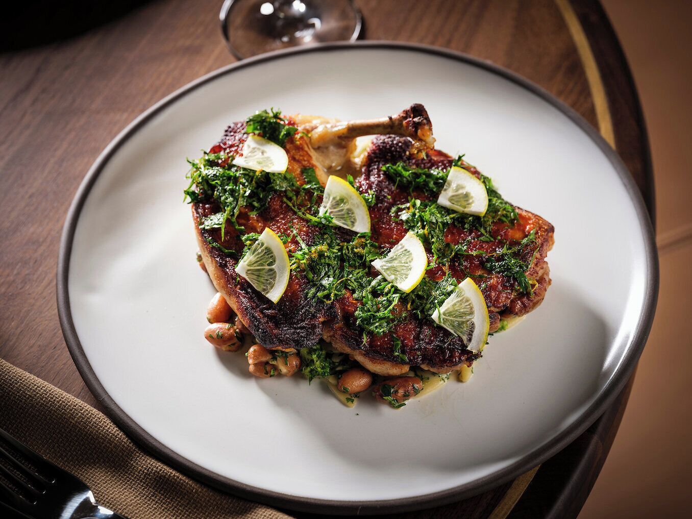 A plate of food with a piece of meat, lemon slices, and herbs.
