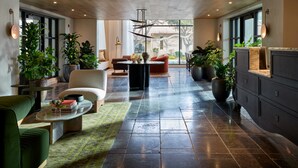 Amplia sala de estar con sofá, sillón y mesa de centro, rodeada de ventanas amplias y plantas en macetas.