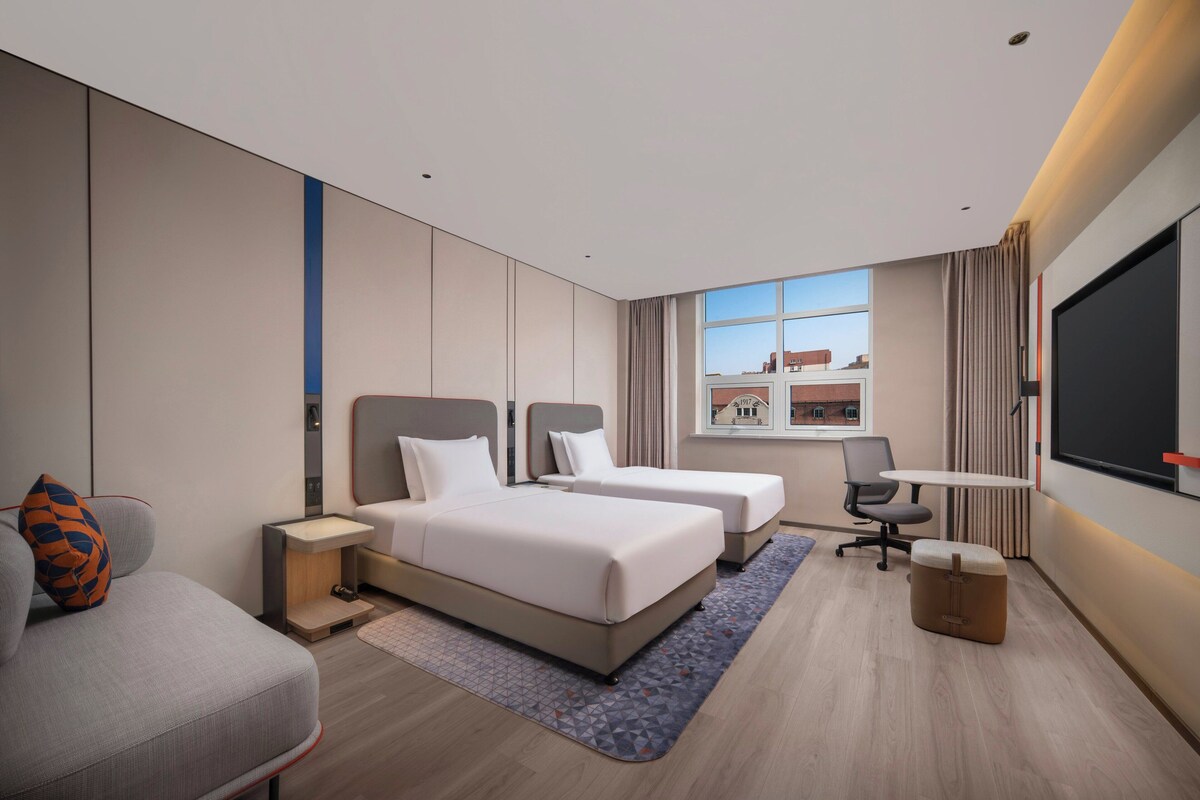 A modern hotel room with two beds, a desk, a chair, and a TV.
