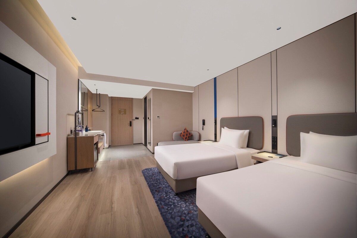 Una habitación de hotel moderna con dos camas, un escritorio, un espejo y un televisor.