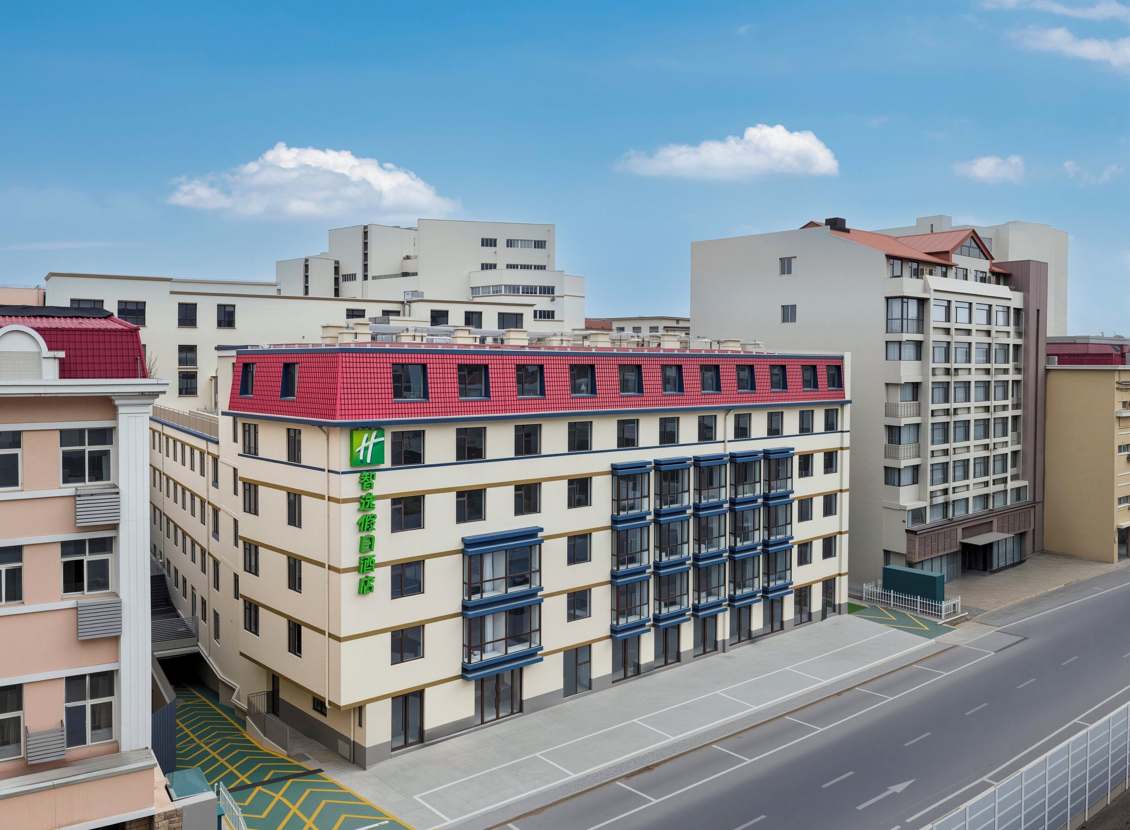 A multi-story hotel with a red roof, beige walls, and a green sign.