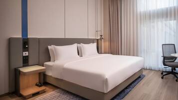 Una habitación de hotel moderna con una cama grande, una mesita de noche, una silla y un ventanal con cortinas.