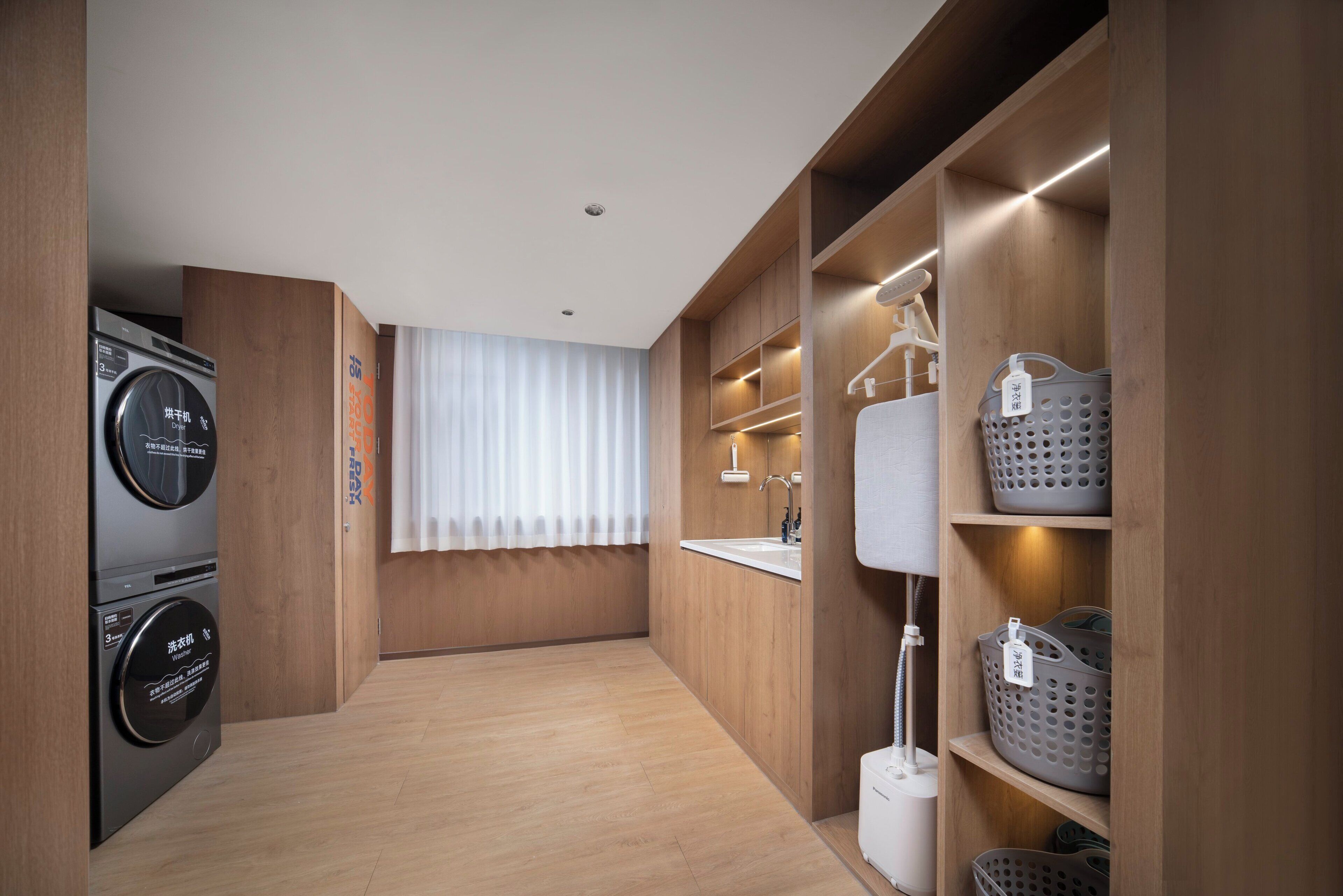 A compact hotel room with a washing machine, a sink, and laundry baskets.