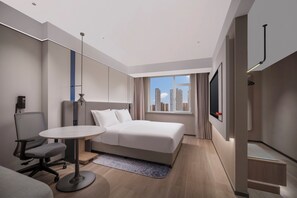 A modern hotel room with a large bed, a desk, a chair, and a view of the city skyline. - Holiday Inn Express Qingdao Downtown by IHG (Qingdao)