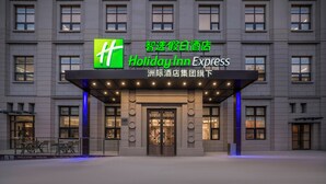 A Holiday Inn Express building with a prominent green logo, a covered entrance, and a tiled ground floor. - Holiday Inn Express Qingdao Downtown by IHG (Qingdao)