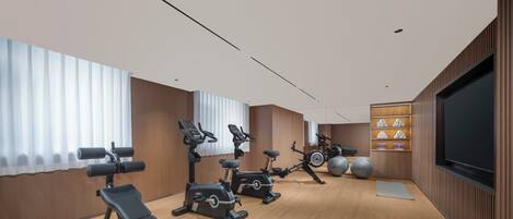 A modern gym with cardio machines, a bench, and a large screen.