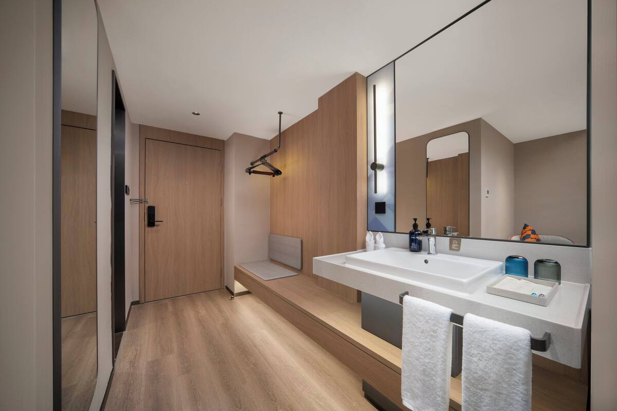 A modern bathroom with a large mirror, two sinks, and a bench.