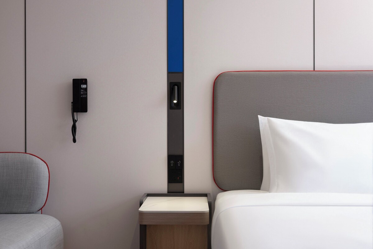 Una habitación de hotel con una cama, una mesita de noche, un teléfono y un panel de control en la pared.
