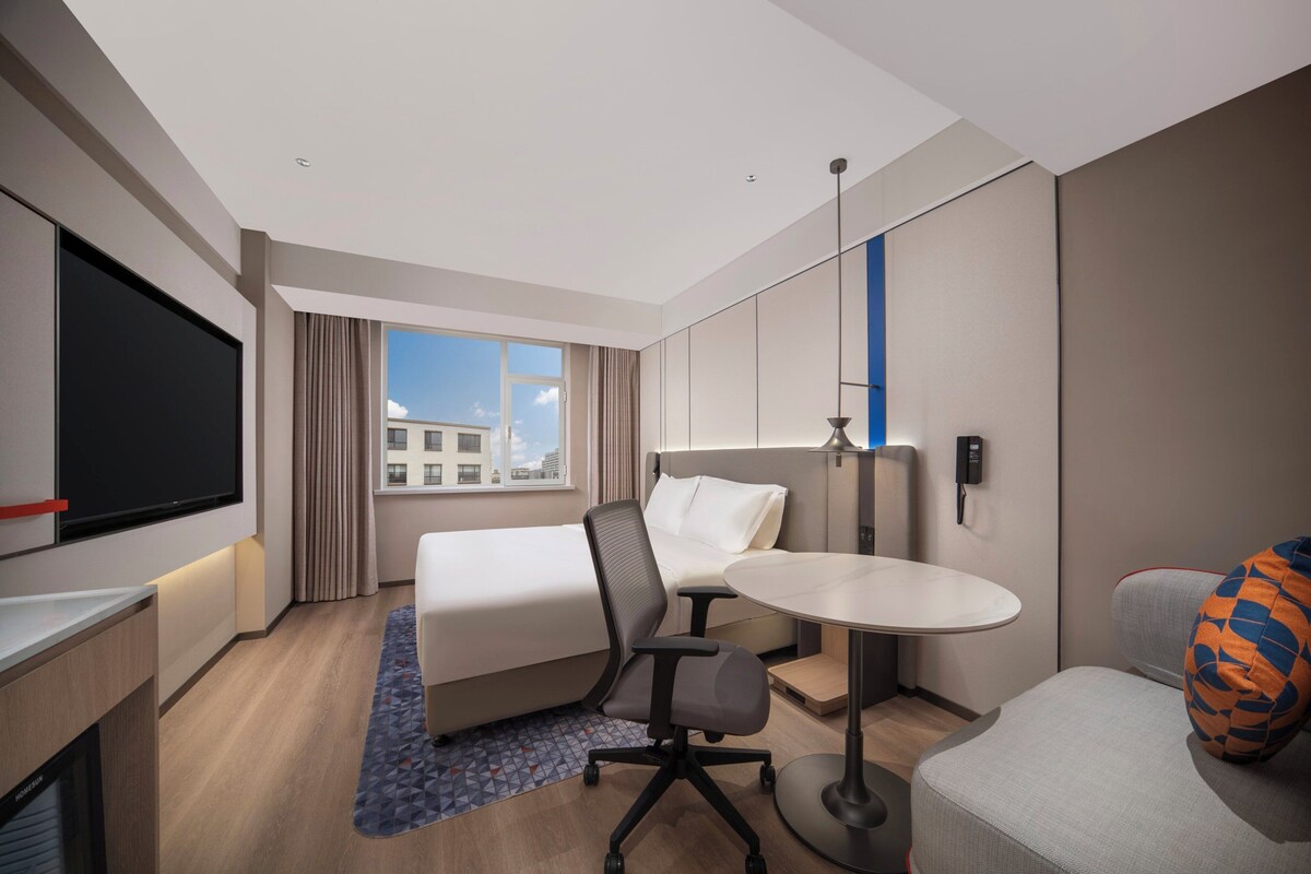 Una habitación de hotel moderna con cama, escritorio, silla y una mesita.