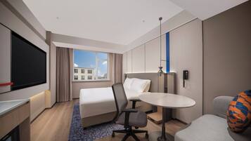 A modern hotel room with a bed, desk, chair, and a small table.